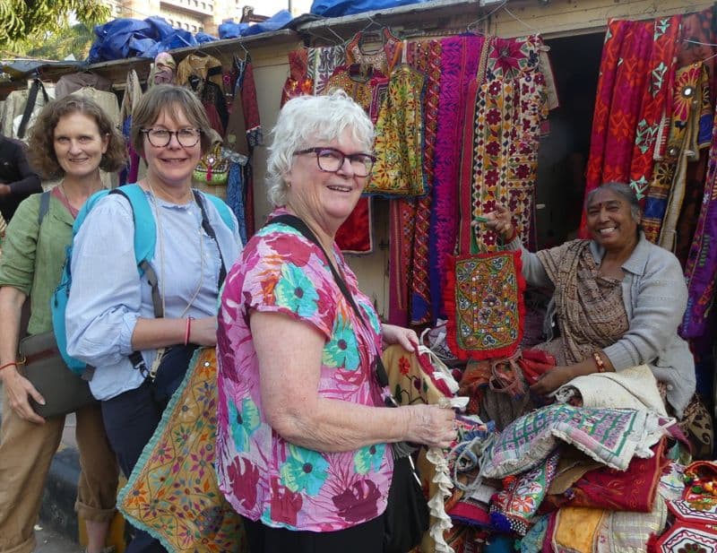3 ladies shopping in textile market with India lady showing textiles